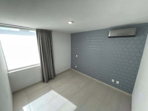 Ein Zimmer mit einem großen Fenster, grauen Vorhängen, einer Wand mit Muster und einer Klimaanlage.