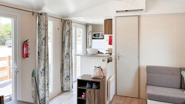Una stanza con soffitto in legno, angolo cottura, divano grigio e porta che dà su uno spazio esterno.
