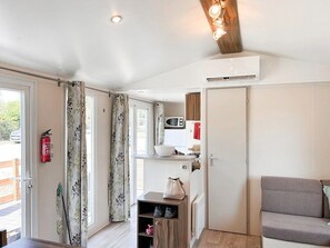 A room with a wooden ceiling, a kitchenette, a grey sofa, and a door leading to an outdoor area. - Unit 1 – Tournesols
Spacious, Relaxing, Ready for Your Next Holiday (Lévignac-de-Guyenne)