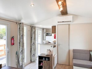 Una habitación con techo de madera, kitchenette, sofá gris y puerta con extintor.