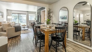 Una sala moderna con un sofá, una mesa de comedor para seis personas y un espejo grande que refleja la habitación.