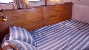 Een enkel bed met een gestreept dekbed en kussens, een houten hoofdbord en een raam met gordijnen.