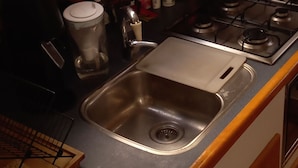 Een kleine keuken met een spoelbak, fornuis en diverse keukengerei.