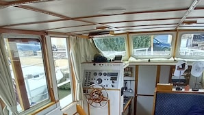 Bootinterieur met een houten tafel, een stuurwiel en een blauw gestoffeerd gedeelte.