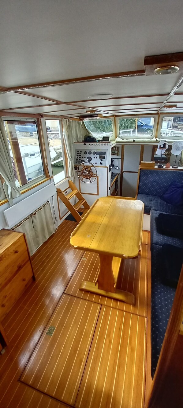 L'intérieur d'un bateau, avec une table en bois, un volant et un espace rembourré bleu.