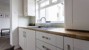 Una cocina con ventana, armarios blancos, un lavamanos y una encimera.