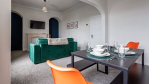 Un comedor con una mesa dispuesta para cuatro personas, un sofá verde y una silla naranja.