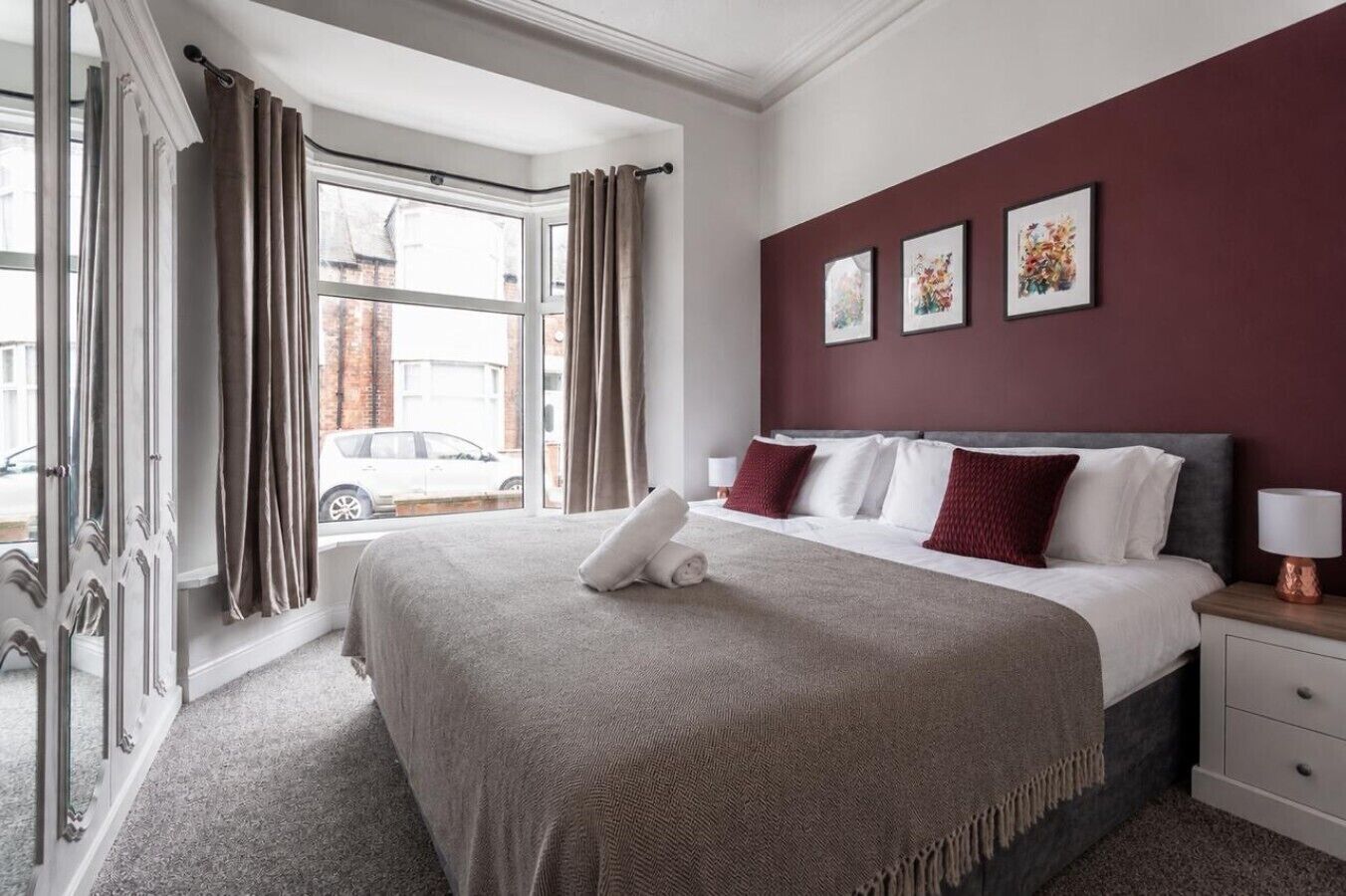 Una habitación de hotel con una cama grande, una mesita de noche, una lámpara y una ventana con cortinas.