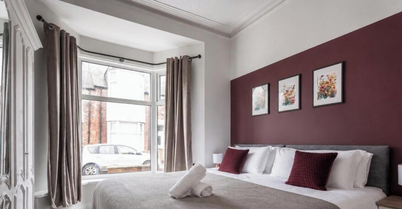 A hotel room with a large bed, a window with curtains, and three framed pictures on the wall.
