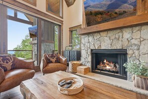 Ein gemütliches Wohnzimmer mit Ledersofas, einem Kamin und einem großen Fenster mit Blick auf eine reizvolle Landschaft.