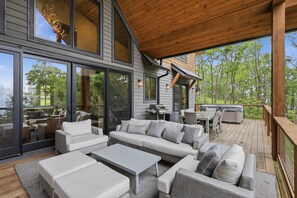 A covered outdoor living area with a wooden deck, a large sofa set, and a grill. - LUX Cabin – Hot Tub, Massive Deck & Mountain Views! (Banner Elk)