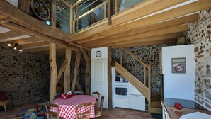 A rustic kitchen with exposed wooden beams, a stone wall, a checkered tablecloth, and a small refrigerator. - “L'air De Vacances” Cottage with Private Terrace and Wi-Fi (Bonnée)