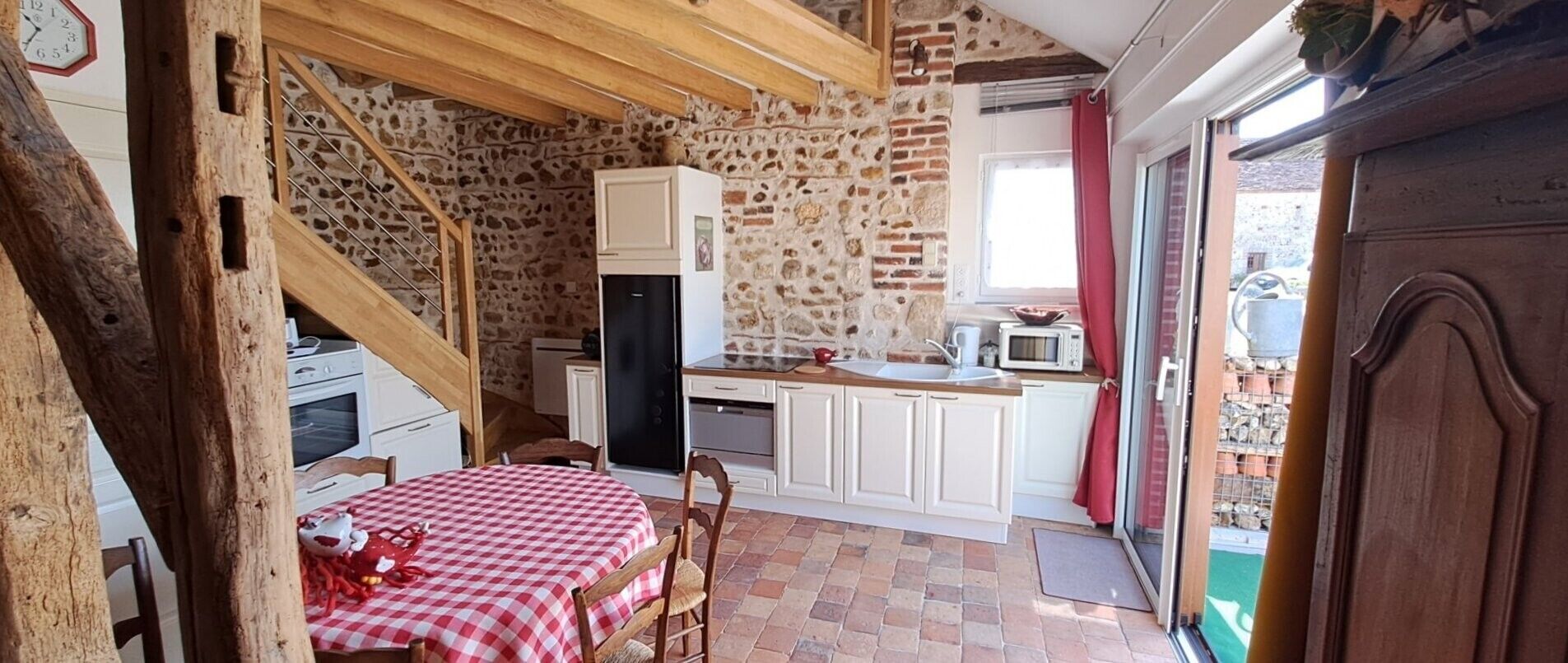Una cucina rustica con parete in pietra, travi in legno, tovaglia a scacchi e una sedia rossa.