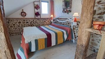 Un dormitorio acogedor con pared de piedra, una cama con manta a rayas de colores, cabecera de madera y una mesita con plantas en macetas.