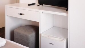 Ein Hotelzimmer mit weißem Schreibtisch, Fernseher, Pouf und weißem Schrank.
