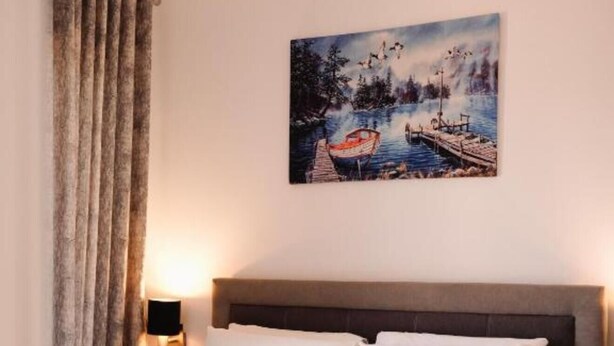 Ein Hotelzimmer mit Bett, einem Bild einer Seelandschaft, einem Nachttisch und einer Lampe.