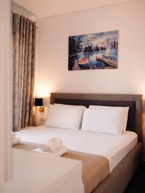 Una habitación de hotel con una cama, un cuadro de un paisaje lacustre, una mesita de noche y una lámpara.