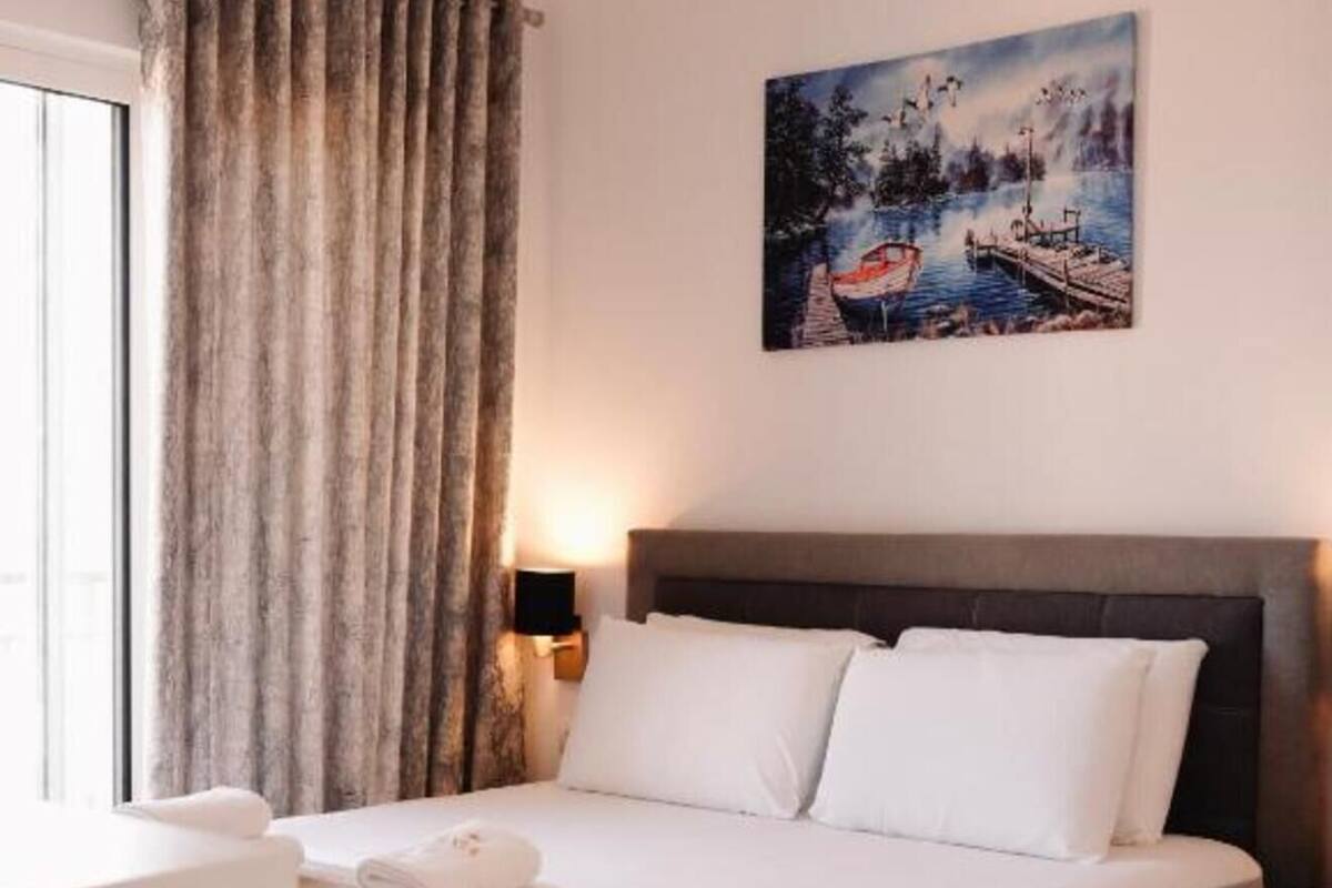 Una habitación de hotel con cama, un cuadro, una ventana con cortinas y una lámpara de noche.