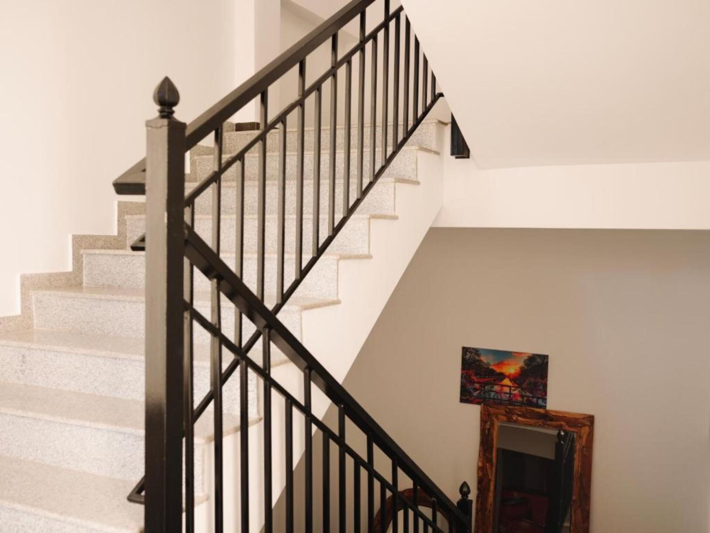 Un escalier avec une rampe noire et un tableau accroché au mur.