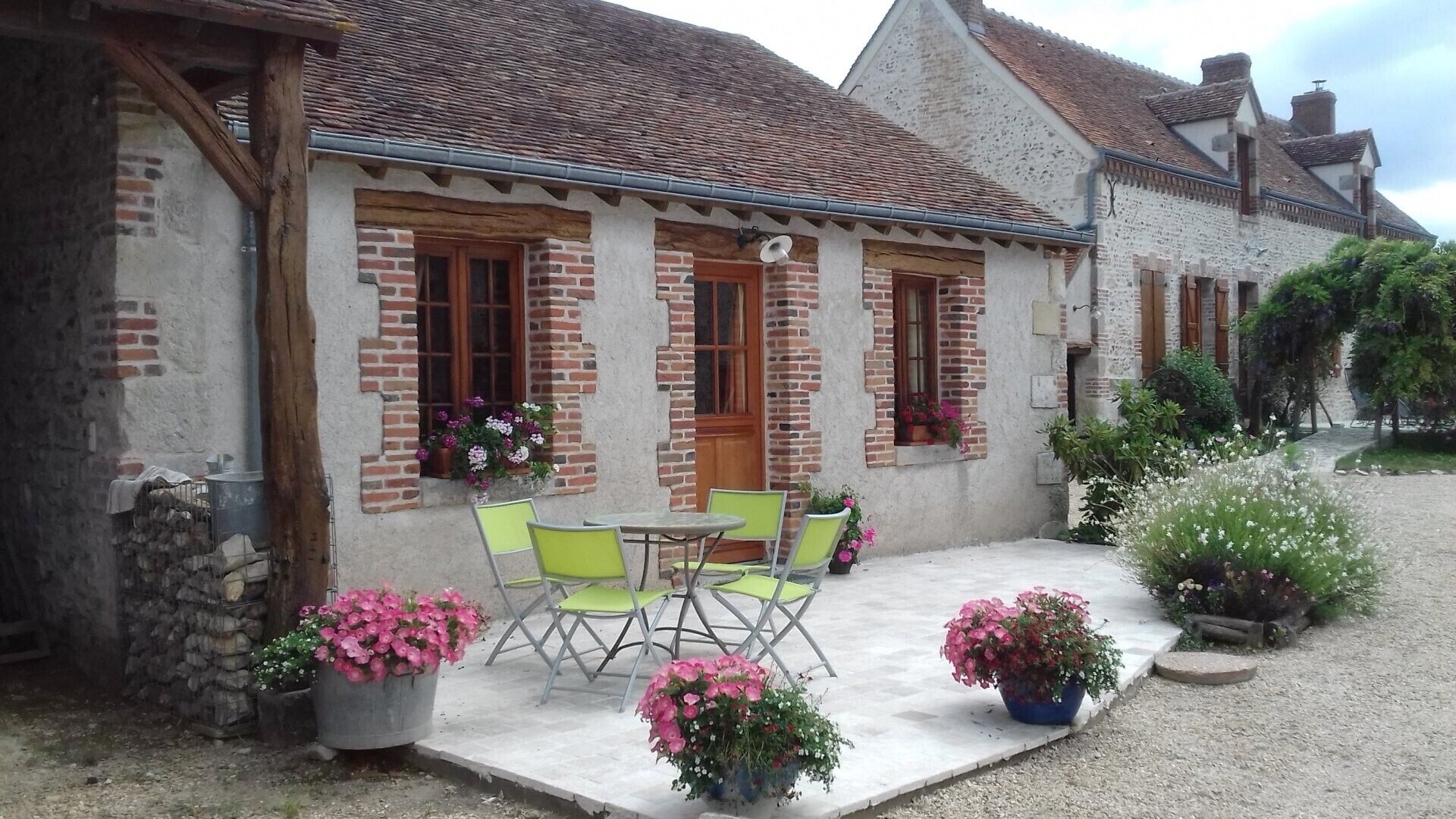 Un bâtiment de style rustique, avec une façade en briques, une porte en bois et un petit patio agrémenté d’une table et de chaises.