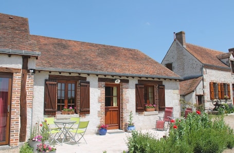 A traditional stone house with a tiled roof, wooden shutters, and a small patio with outdoor seating.. Bed and Breakfast 'L'églantier'