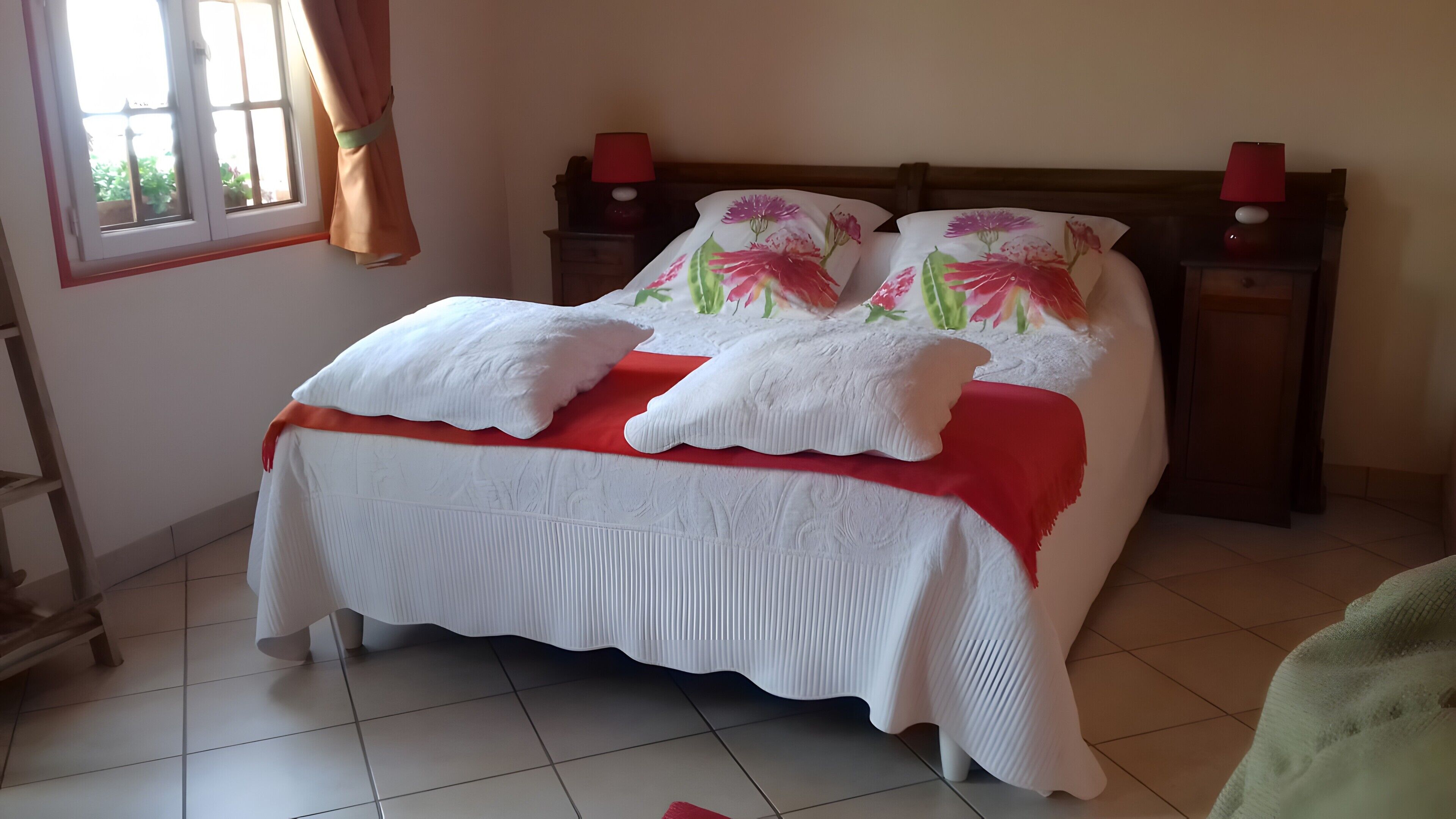 A neatly made bed with white bedding and a red accent, a wooden headboard, and two bedside lamps.