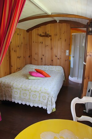 A wooden-paneled room with a bed, a chair, and a door leading to a shower. - Bed and Breakfast 'Roulotte Esméralda' with Balcony, Wi-Fi and Air Conditioning (Bonnée)