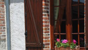 A brick building with a window, a flower box with flowers, and two green chairs. - Bed and Breakfast 'Roulotte Esméralda' with Balcony, Wi-Fi and Air Conditioning (Bonnée)