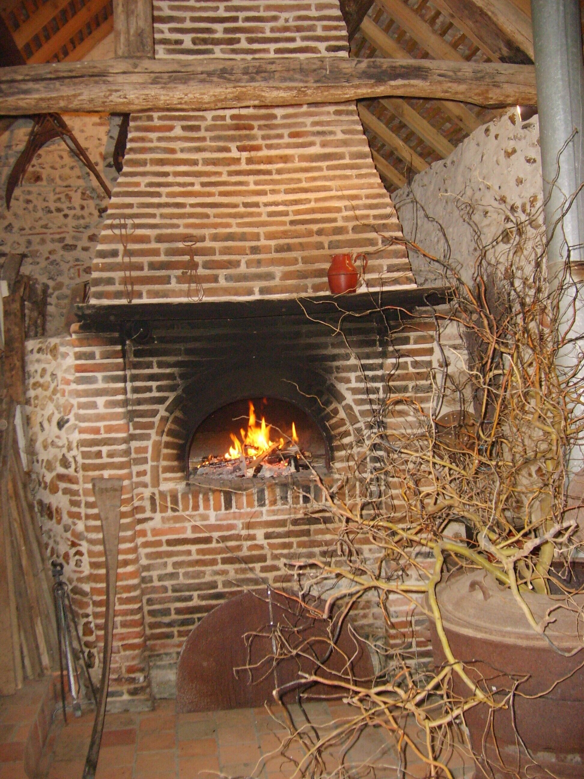 A brick fireplace with a fire burning, surrounded by stone walls and wooden beams.