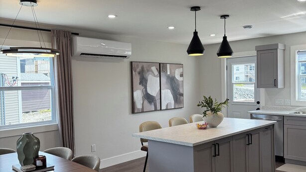 A modern kitchen with a central island, pendant lighting, and a dining area with chairs and a table.