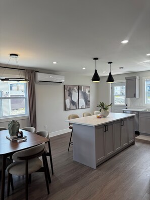 A modern kitchen with a central island, pendant lighting, and a dining area with chairs and a table.