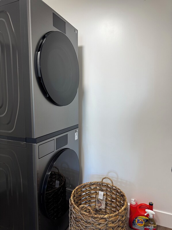 A front-loading washer and dryer unit with a basket and Tide detergent nearby. - The Aiyra Residence | 2 Kings| Patio| Parking (St. John's)