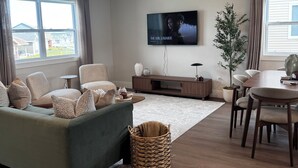 A modern living room with a sofa, TV, dining table, and a large window.
