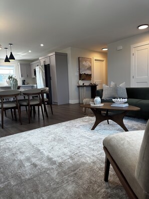 A modern living room with a sofa, a coffee table, and a dining area with chairs and a table.