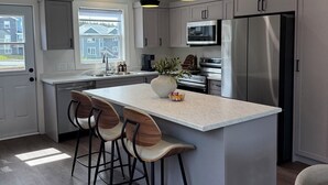 A modern kitchen with a central island, bar stools, stainless steel appliances, and pendant lighting.