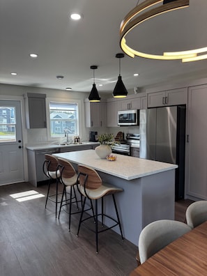 A modern kitchen with a central island, bar stools, stainless steel appliances, and pendant lighting.