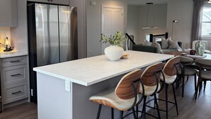 A modern kitchen with a central island, bar stools, pendant lighting, and a stainless steel refrigerator.