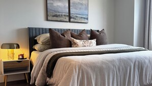 A bedroom with a bed, nightstand, lamp, ceiling fan, and two wall-mounted paintings.