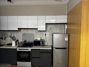 Eine Küche mit weißen Schränken, einem Edelstahl-Kühlschrank, einer Mikrowelle, einem Herd und einem Backofen.