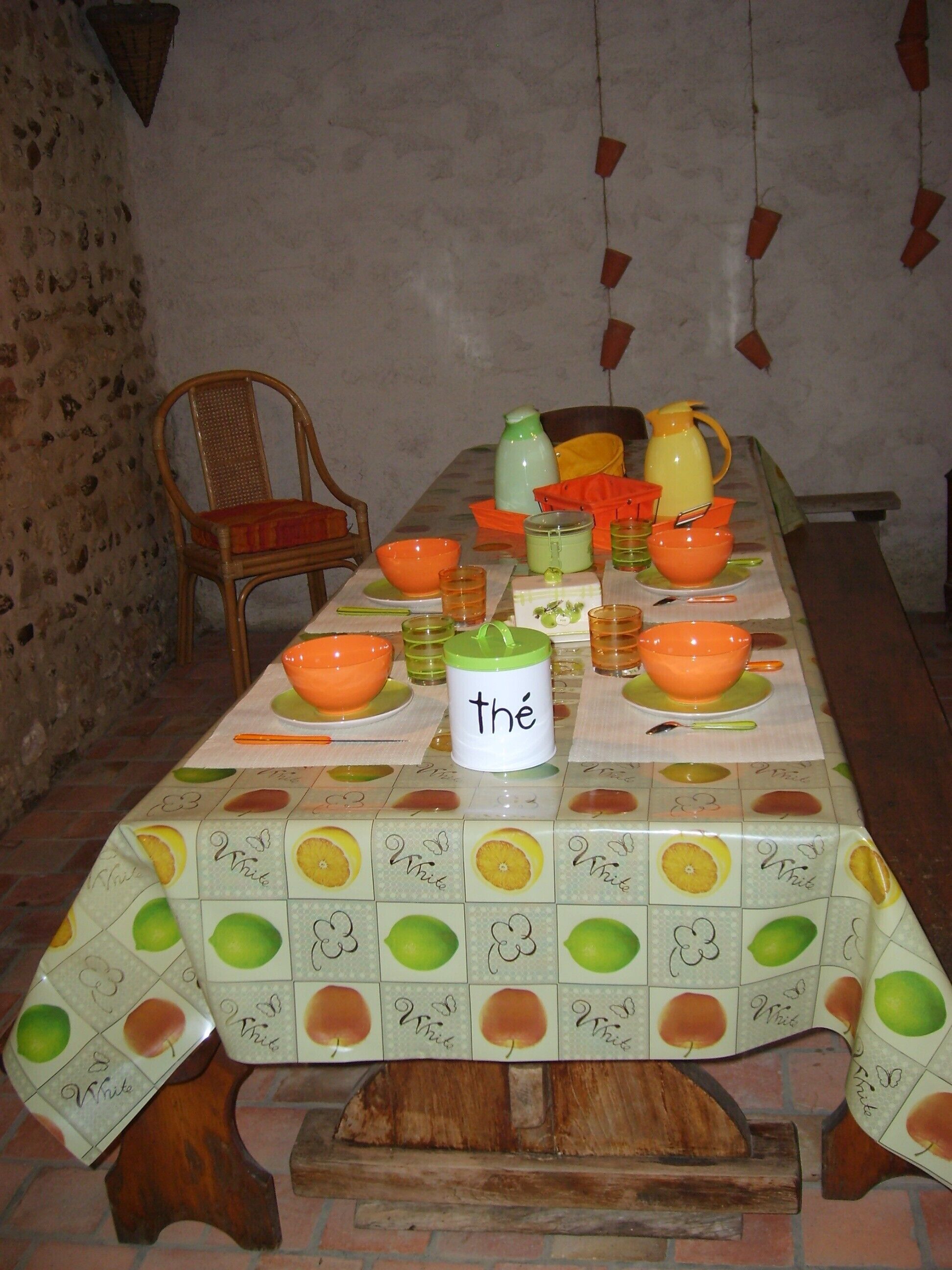 A dining table set with various bowls, cups, and a pitcher, surrounded by a rustic brick wall and a wooden chair.