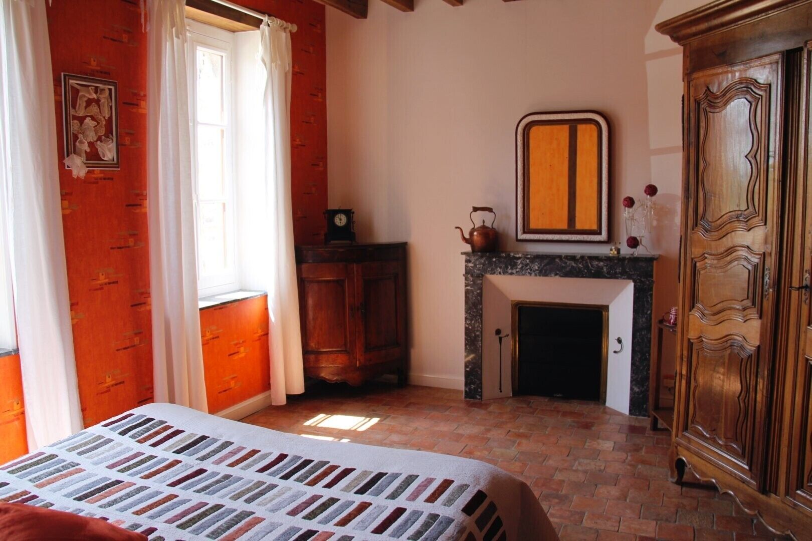 A bedroom with a bed, a fireplace, a wardrobe, and a window with curtains.