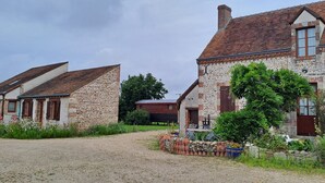 A rural setting with stone buildings, a gravel path, and a garden with various plants and flowers. - Bed and Breakfast 'Volière' with Wi-Fi (Bonnée)