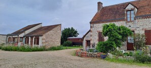 Ländliche Umgebung mit Steinhäusern, einem Kiesweg und einem Garten mit verschiedenen Pflanzen und Blumen.