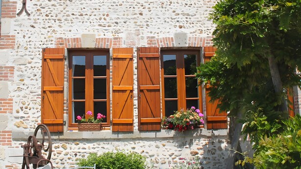 A stone building with a tiled roof, a brick chimney, and a window with wooden shutters. - Bed and Breakfast 'Volière' with Wi-Fi (Bonnée)