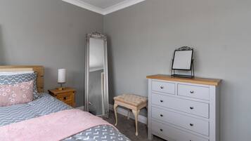 A bedroom with a bed, a nightstand, a dresser, a mirror, and a stool.