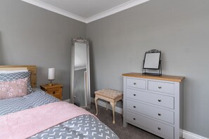 Une chambre à coucher comprenant un lit, une table de chevet, une commode, un miroir et un tabouret.
