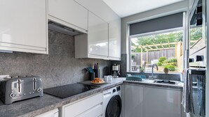 A modern kitchen with white cabinets, a built-in washing machine, a toaster, and a window with a view of the outdoors. - Shepherd's Lodge (Skipton)