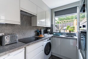 A modern kitchen with white cabinets, a built-in washing machine, a toaster, and a window with a view of the outdoors. - Shepherd's Lodge (Skipton)