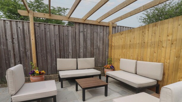 An outdoor patio with a wooden pergola, a sofa set, a coffee table, and potted plants. - Shepherd's Lodge (Skipton)