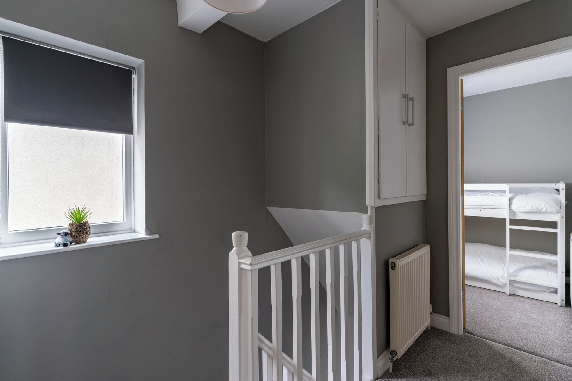 Una habitación con ventana, un radiador, una barandilla blanca y una cama individual.